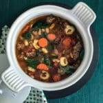 A white soup tureen filled with Italian Sausage and Bean Soup on a green background.