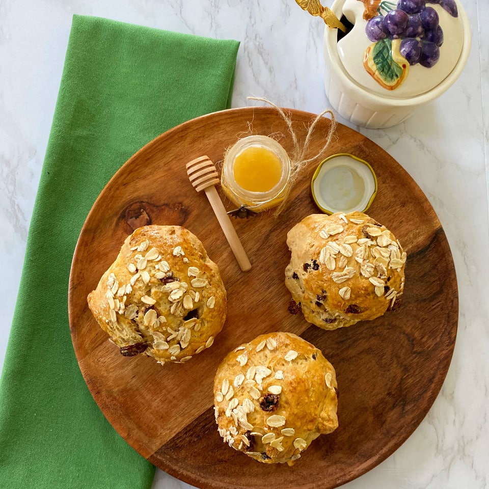 A wooden plate with Irish Soda Bread rolls and a jar of honey