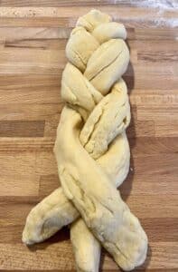 Italian Easter Bread dough rolled in 3 pieces and braided on a wood cutting board