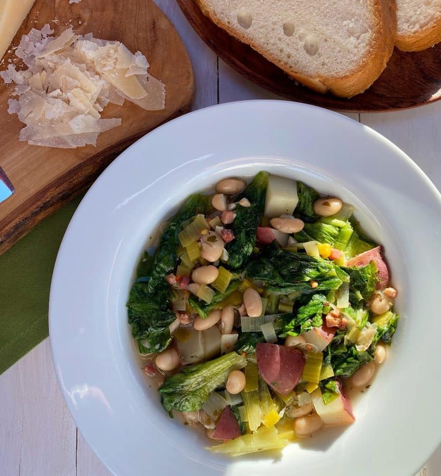 A bowl of beans and greens with Italian bread and Parmesan Cheese