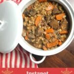A white bowl filled with beef and barley stew on a wood counter with a red and white towel surrounding it.