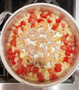Cooked Shrimp in the middle of a saute pan with tomatoes and onions on the side.