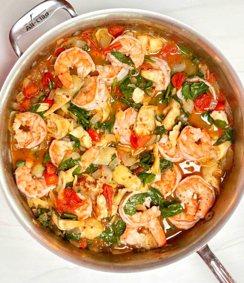 Cooked shrimp with tomatoes, artichokes and spinach in a saute pan 