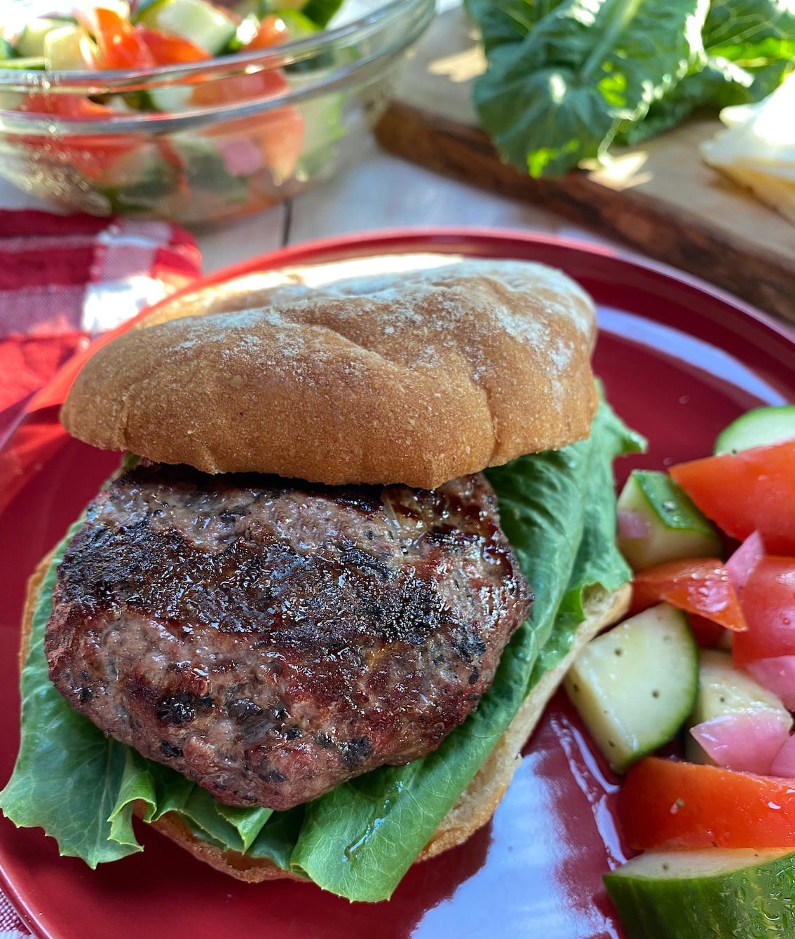 A red plate with a grilled burger on a whole wheat bun with a salad on the side