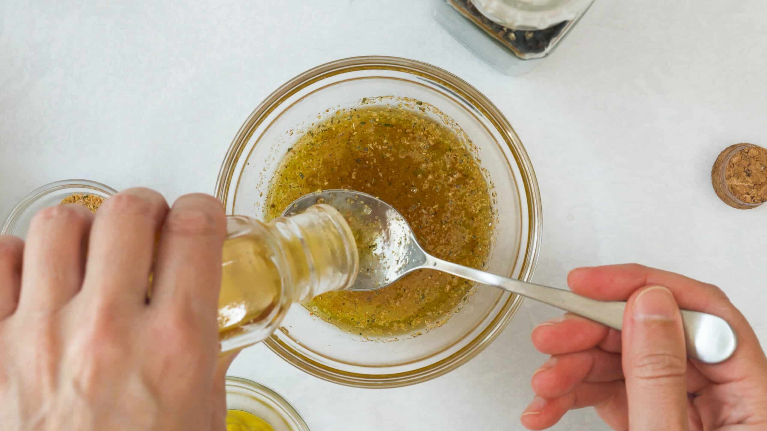 Someones measuring a liquid into a glass jar while making a salad dressing. The jar is on a white counter.