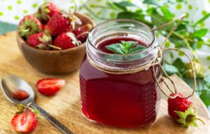 A jar of strawberry simple syrup on a wooden cutting board