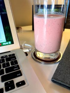 A glass of strawberry watermelon smoothie on desk with a computer