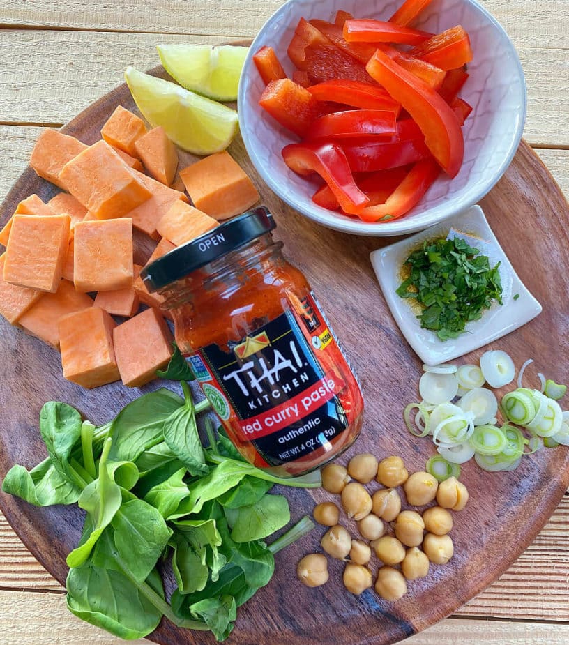 A wooden plate with the ingredients used to make spicy sweet potato and chickpea soup.