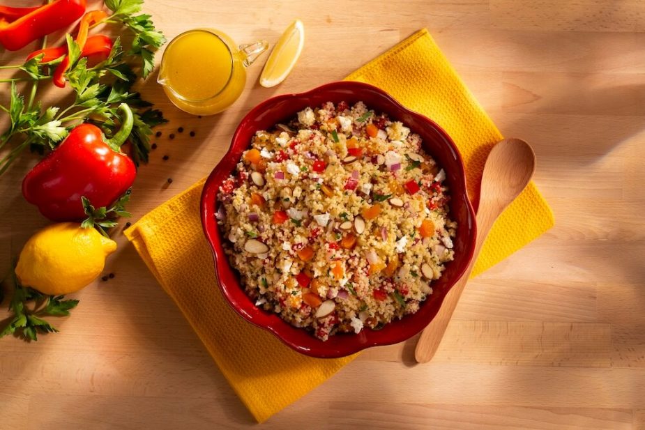 A red bowl filled with Lemon flavored couscous and vegetable salad sprinkled with Almonds