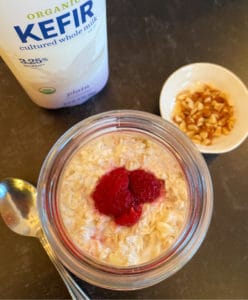 An overhead look at a mason jar filled with oatmeal, kefir and raspberries with almonds on the side.