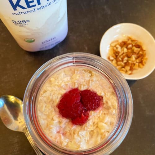 An overhead look at a mason jar filled with oatmeal, kefir and raspberries with almonds on the side.