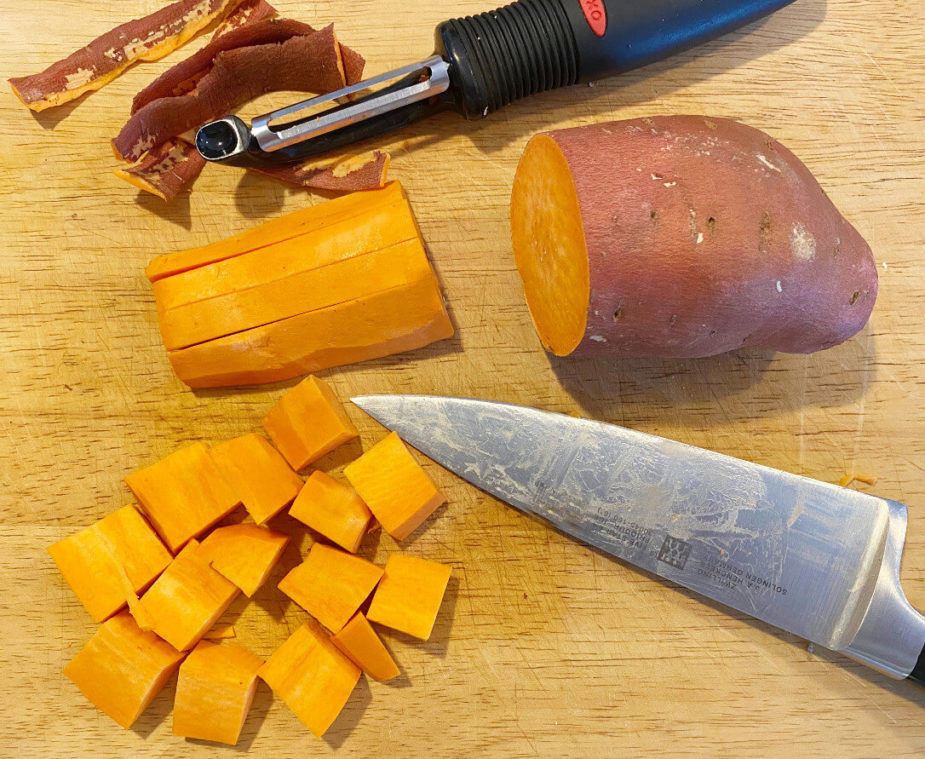 A partially cut sweet potato on a wooden cutting board with a knife. 
