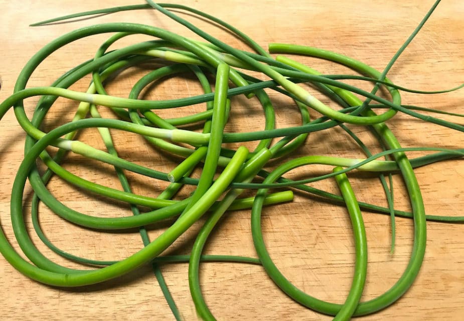 A pile of garlic scapes on a wooden cutting board