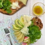 A glass plate filled with watercress, pears and avocados on a white picnic table