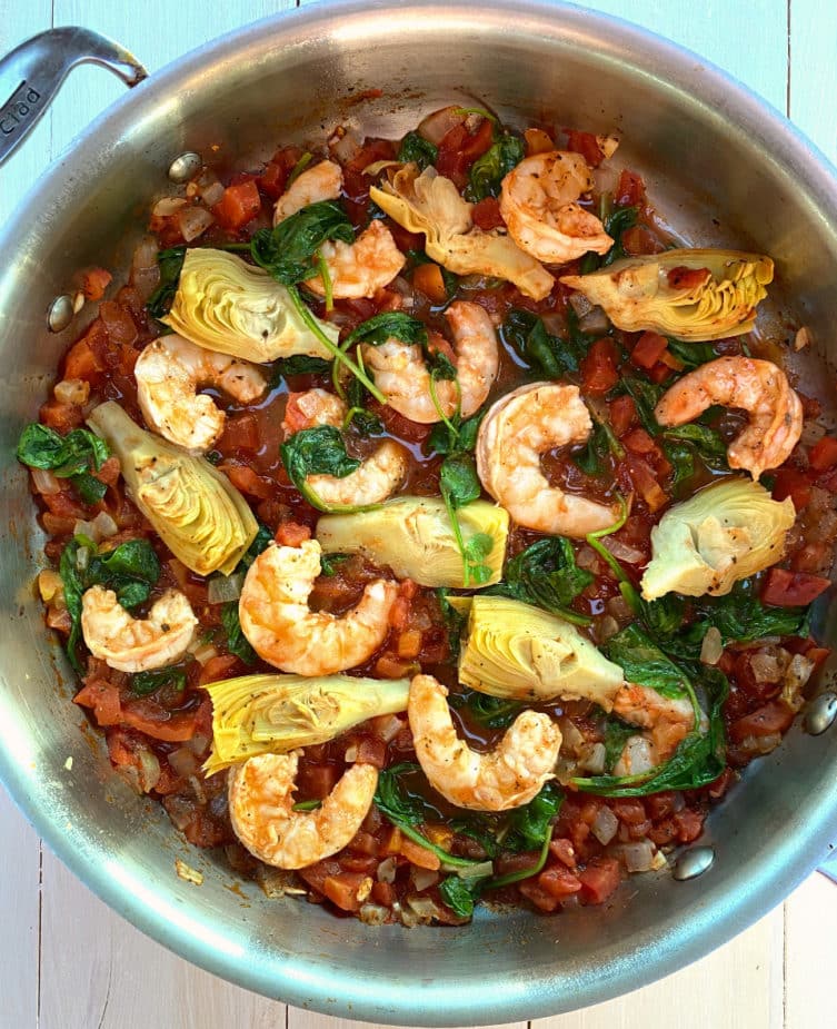 A pan of shrimp in tomato sauce with artichokes and spinach