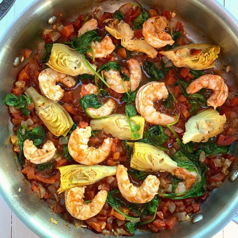A pan of shrimp in tomato sauce with artichokes and spinach