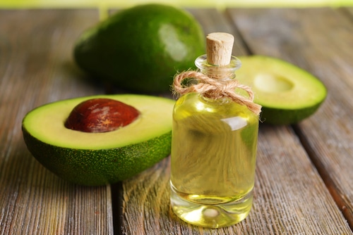 Avocado oil and a sliced avocado on a dark wood picnic table