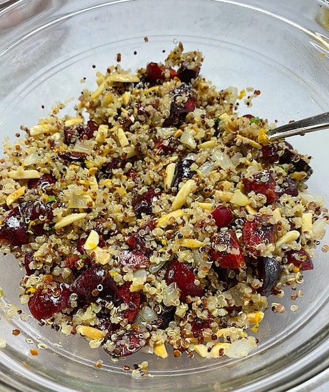 A glass mixing bowl with quinoa, cherries, almonds and onions.