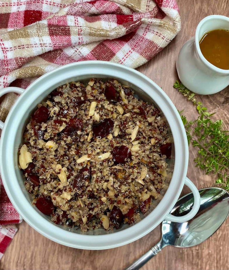 A white bowl filled with a quinoa salad with fresh cherries and toasted almonds. Citrus vinaigrette is on the side