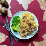 A white plate with roasted chicken and grapes over egg noodles with broccoli