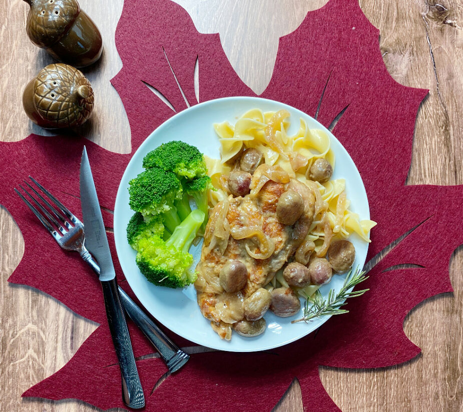 A plate of chicken with roasted grapes, egg noodles and broccoli on a red leaf placemat