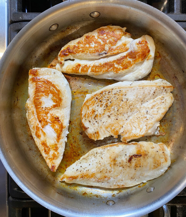 Browned chicken breasts in a saute pan on a stovetop