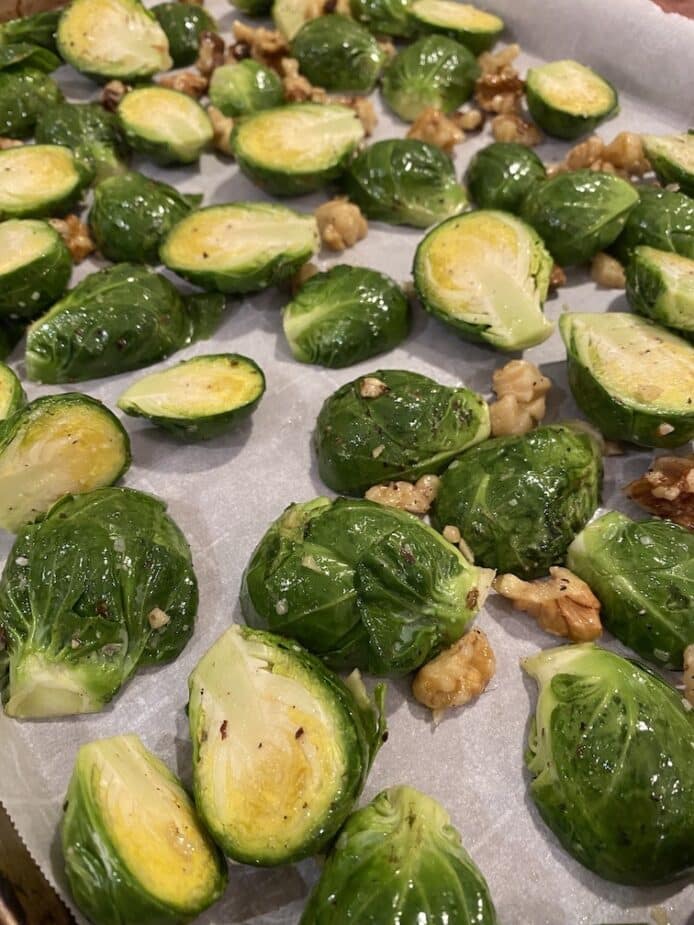 Brussel sprouts and walnuts on a parchment paper lined sheet pan ready to go in the oven