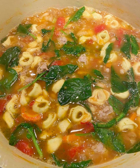 Italian sausage and white bean soup in the final stage of cooking. Baby spinach added and just beginning to wilt.