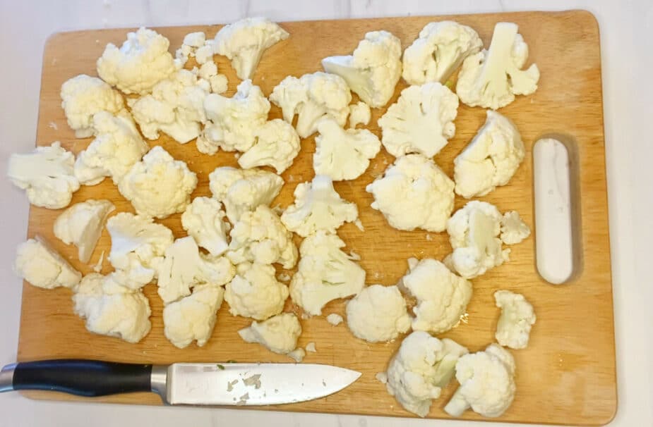 Cauliflower cut into ~ 2 inch pieces on a wood cutting board
