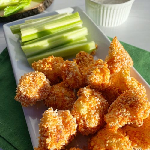 A white plate with buffalo cauliflower bites and celery sticks