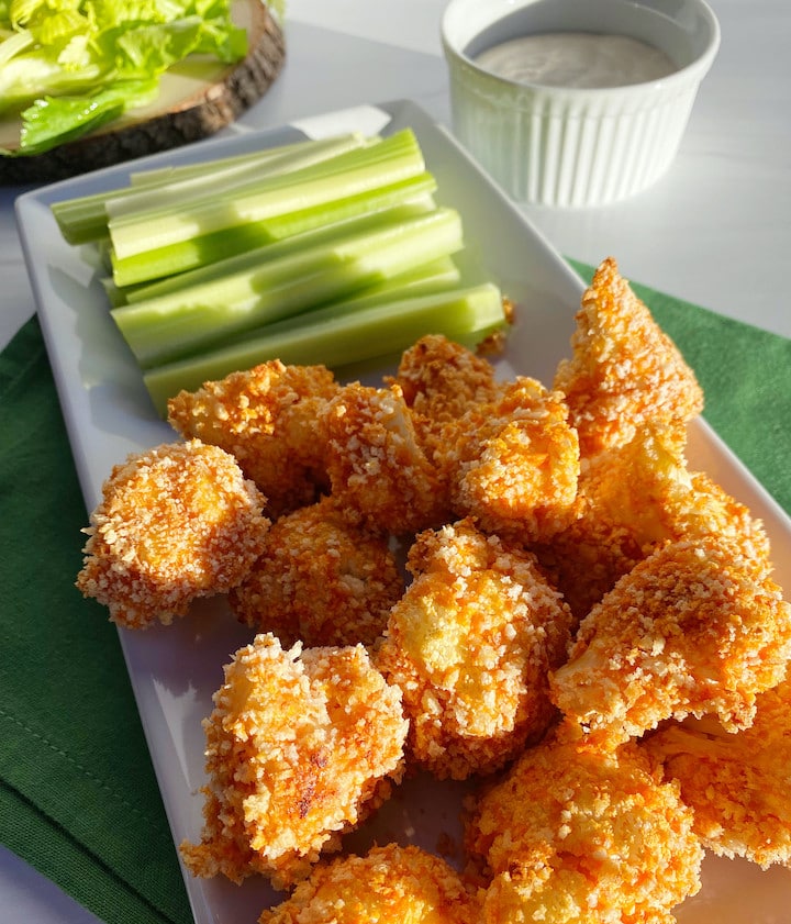 A white plate with buffalo cauliflower bites and celery sticks