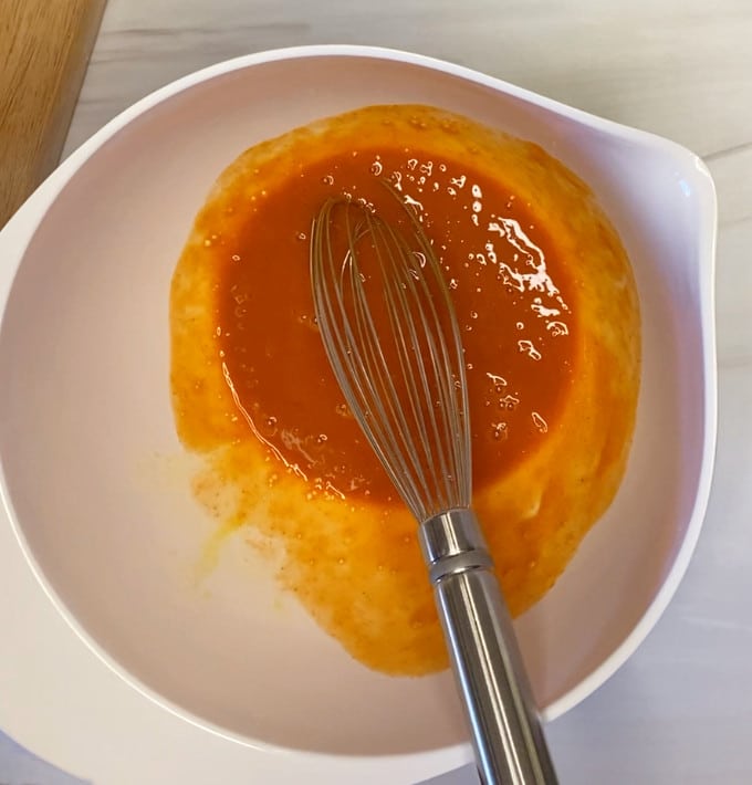 Egg whisked with hot Buffalo sauce in a white bowl.