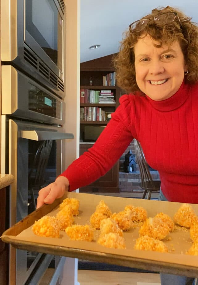 Woman holding a baking sheet with hot Buffalo coated cauliflower pieces ready to cook in the oven