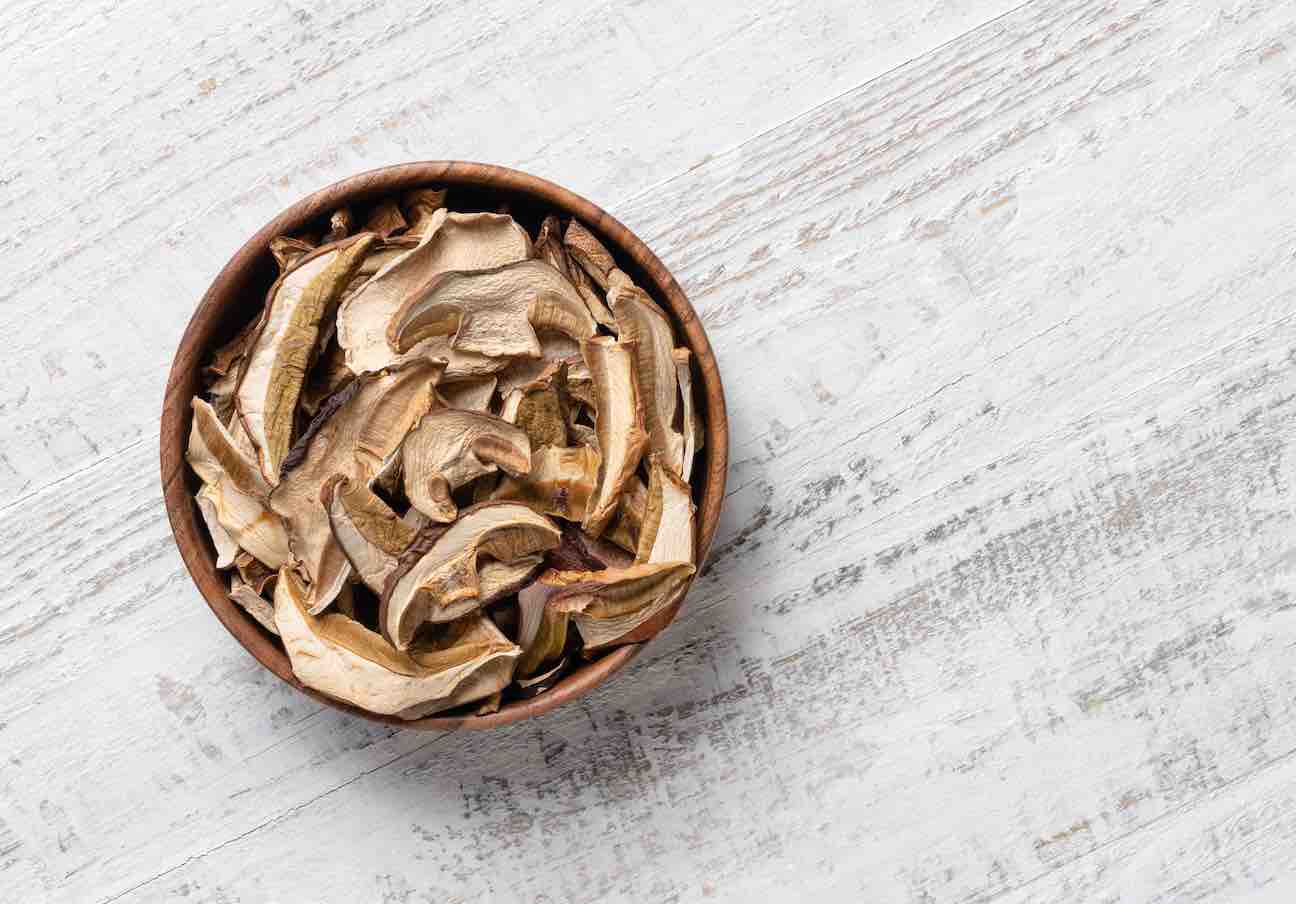 Dried porcini mushrooms in  wooden bowl on white wooden table. overhead view.  