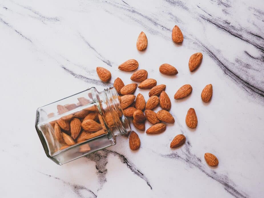 A jar of almonds spilled over on a white marbled counter top