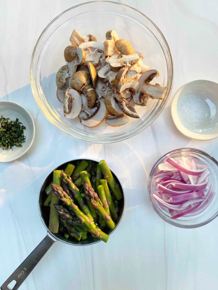 Ingredients prepped and ready to make the asparagus mushroom saute sitting on a white marble countertop.