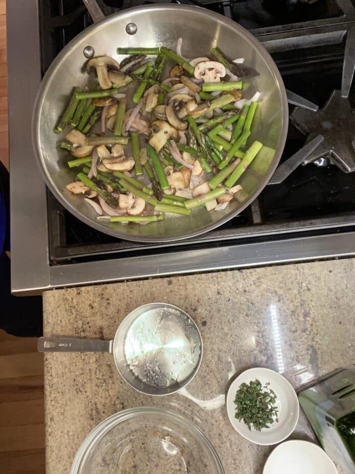 Asparagus mushroom saute cooking is a large saute pan on a stove top.