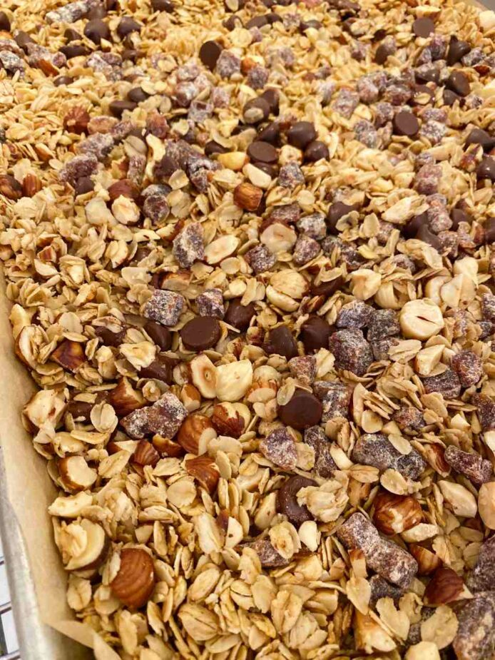 Granola in a pan lined with parchment paper with dates and chocolate chips on top.