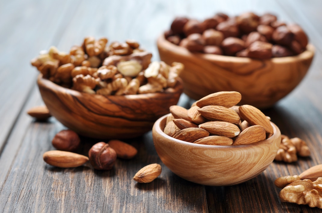 3 wooden bowls of almonds, walnuts and hazelnuts on a dark wood table