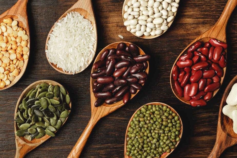 Dry beans are good food for your mood! 8 large wooden spoons each filled with a different type of bean or seed on a wooden table