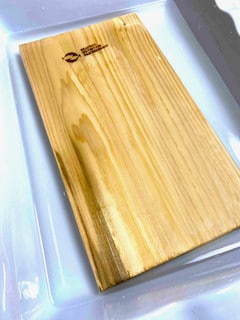 A cedar plank soaking in a large pan filled with water