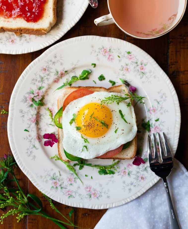 Sunny side up egg to help boost your mood is on a piece of toast with tomato and greens on a china plate on a wood table