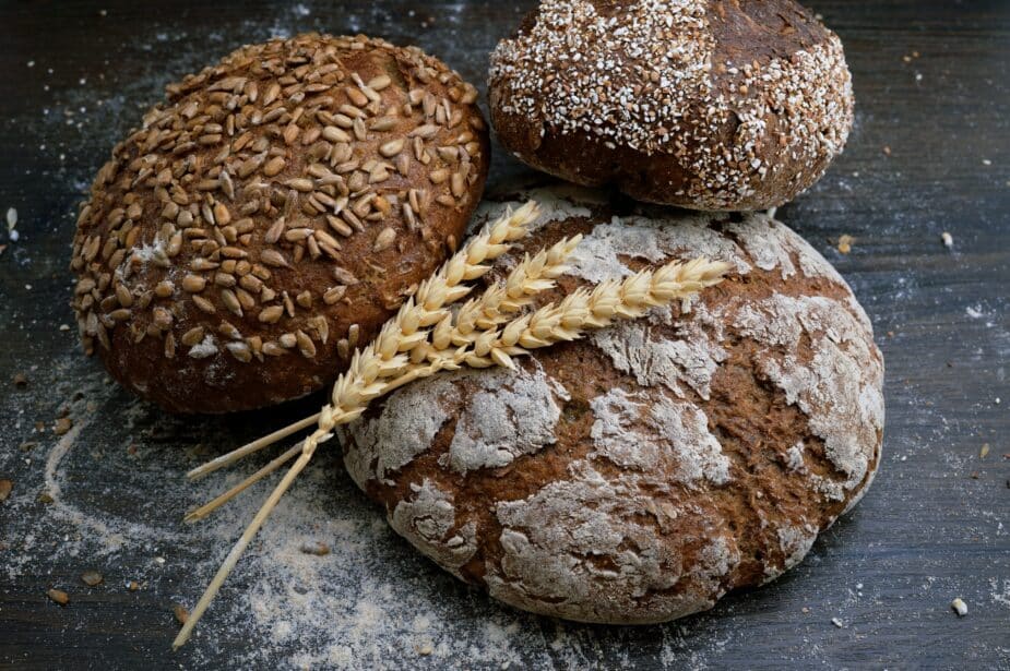 Whole grain buns with some wheat stalks on a black table with flour on the surface