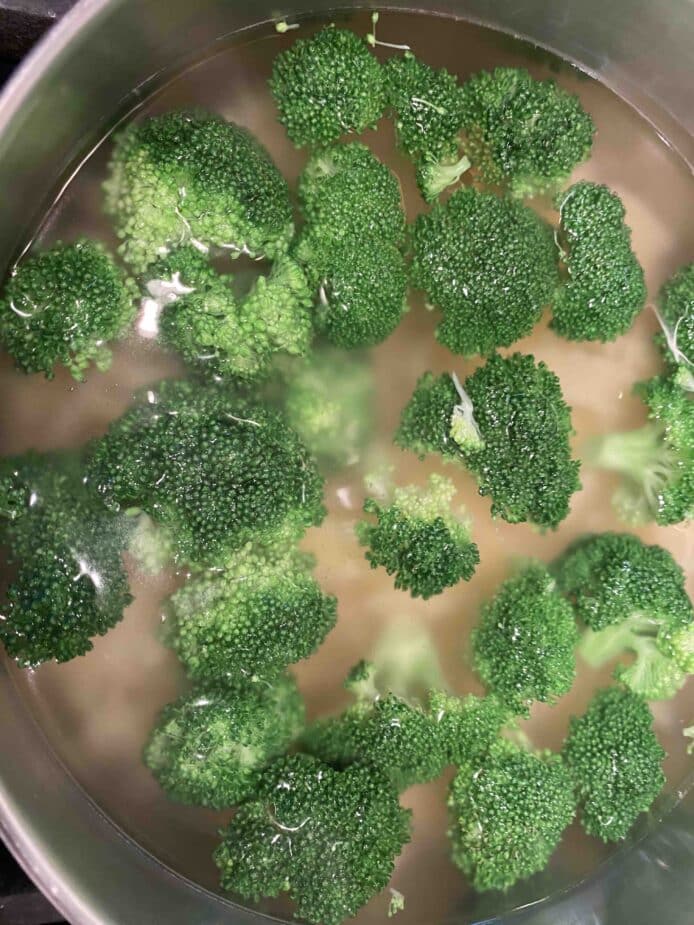 Broccoli cooking in a pan of water with pasta.