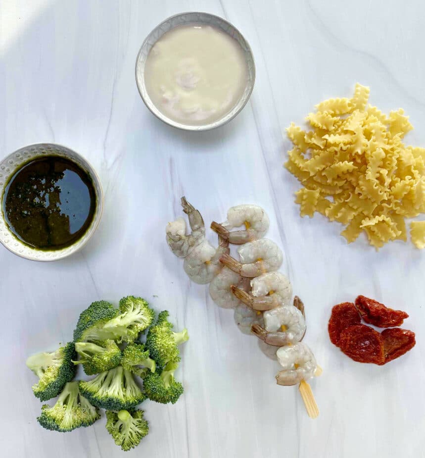 Ingredients for Grilled Shrimp and Pesto Pasta salad on a white marble counter