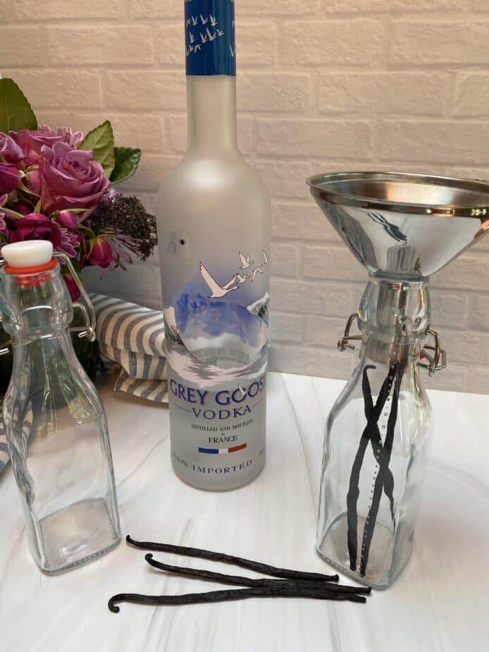 Clear bottles with a snap - top lid, vanilla beans and a bottle of vodka sitting on a marble counter top.