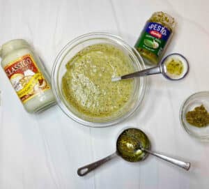 Pesto alfredo sauce on a marble counter with a jar of alfredo sauce and pesto sauce on the side.
