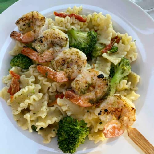 Pesto pasta salad in a white bowl with a skewer of grilled shrimp placed on top
