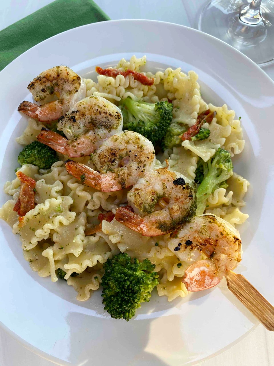 Pesto pasta salad in a white bowl with a skewer of grilled shrimp placed on top