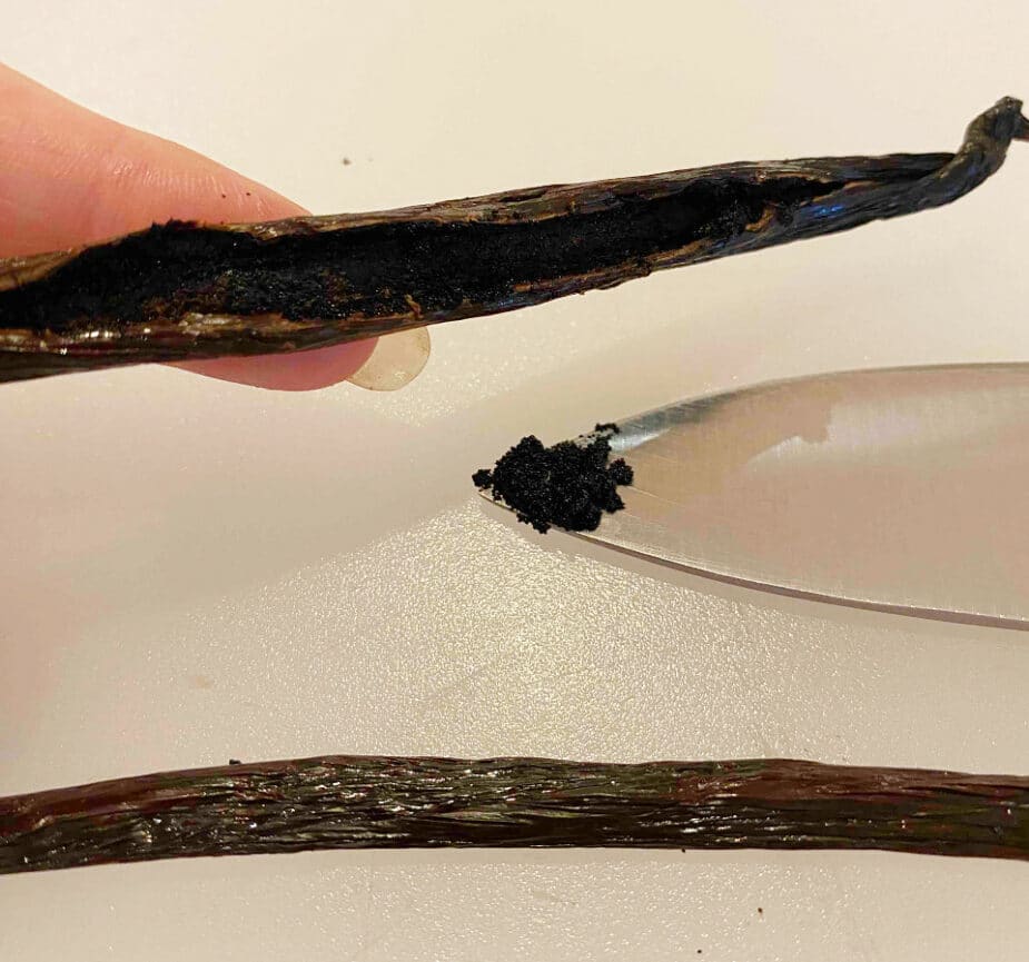 A sliced open vanilla bean pod with the inside scraped out and on the tip of a knife. This is called vanilla "caviar"
